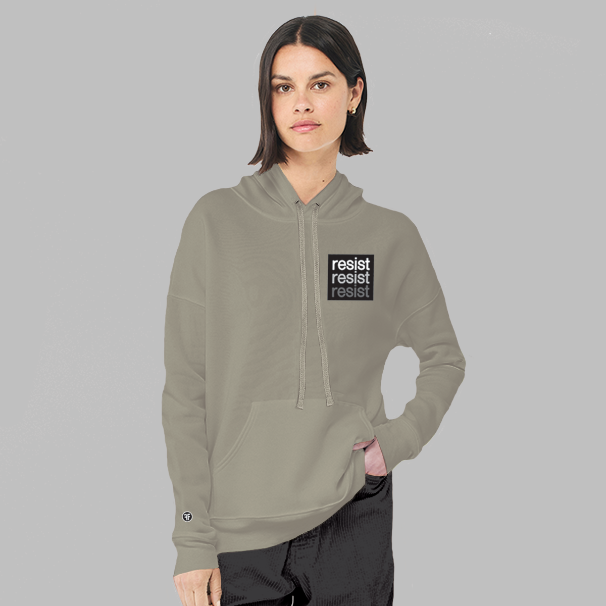 A lady wearing a stone taupe, unisex political hoodie. The logo is a left chest black square, with text that says Resist, three times in white, light grey and dark grey.
