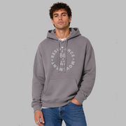 A man wearing a slate purple colored, unisex political hoodie. The grey text says "86 47"in the middle with"Resistance Movement" around it.