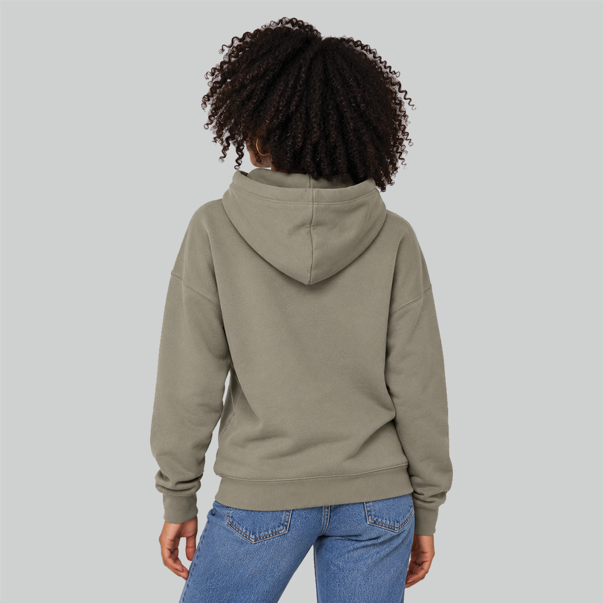 A lady shown from the back wearing an oversized pullover hoodie in a muted stone taupe color, paired with blue jeans, against a solid light gray studio background.