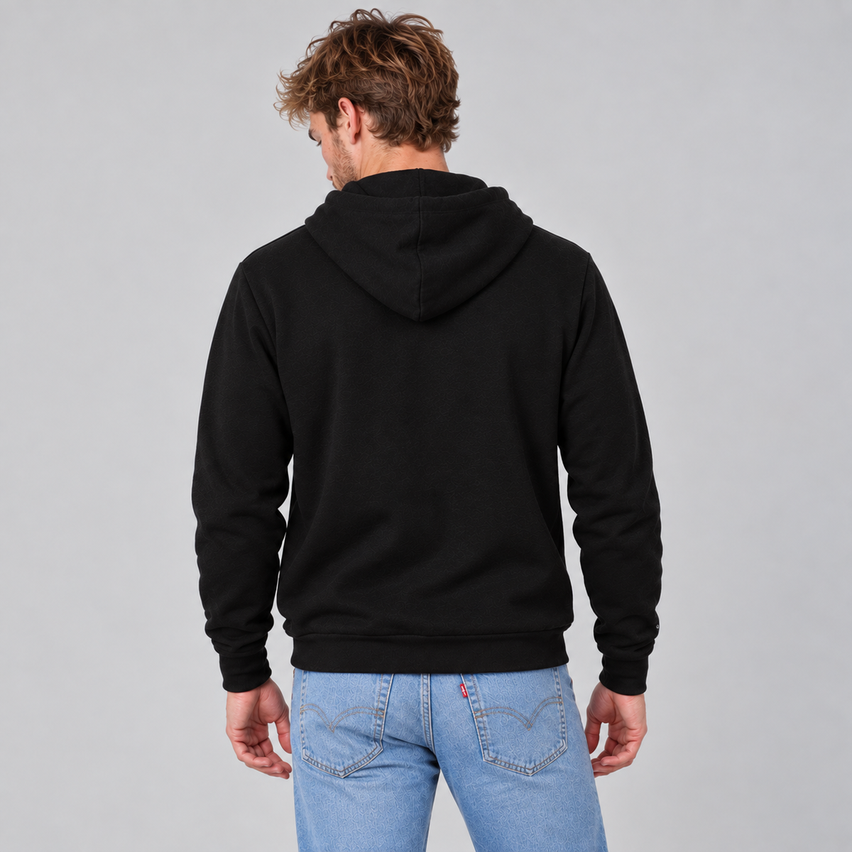 A man viewed from behind wearing a black pullover hoodie showing a unisex fit and that there are no graphics or logo on the back.