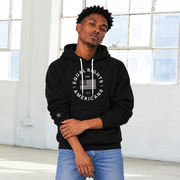 A man wearing a black pullover hoodie with a white circular 'Equal Rights for Americans' graphic on the chest, paired with blue jeans, standing in a bright, white-walled room with large industrial windows.