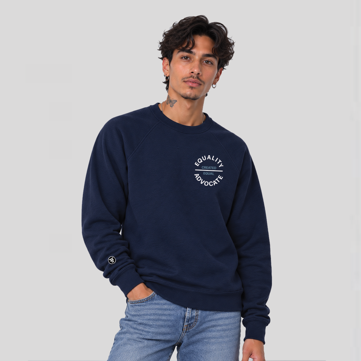A man wearing a navy blue crewneck sweatshirt with a white circular 'EQUALITY ADVOCATE ' graphic on the left chest with 'CREATED EQUAL' in the center of it in stone bllue