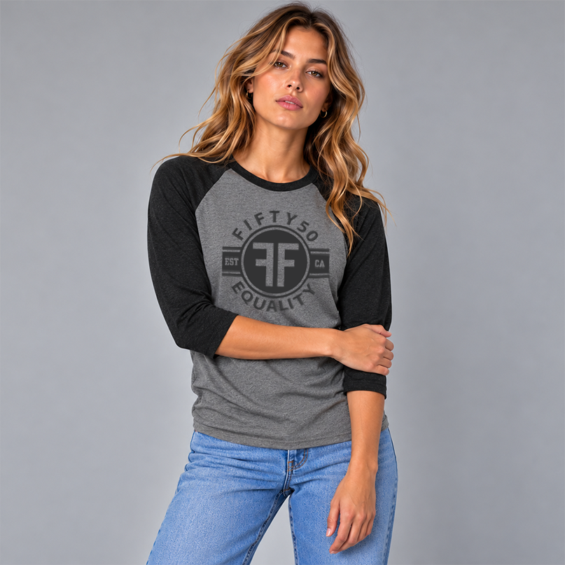 A woman wearing a heather grey equality baseball t-shirt with heather black arms and collar. The text of the black graphic says Fifty50, Equality, and has two Fs, back to back in a circle.