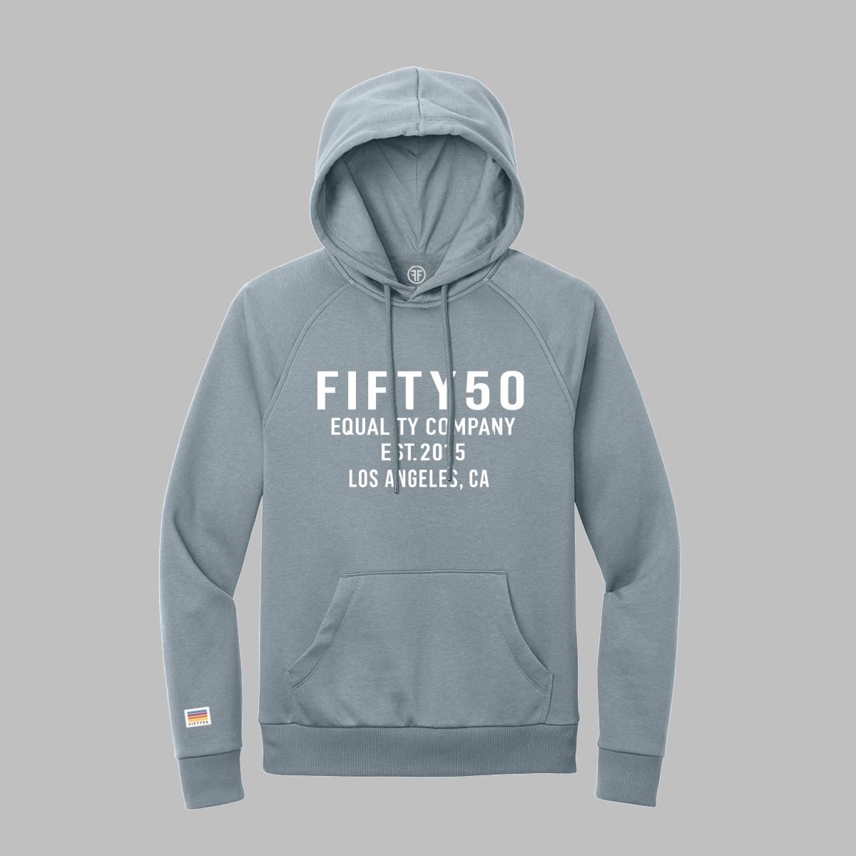 A slate blue pullover hoodie with white text on the chest reading 'FIFTY50 EQUALITY COMPANY EST. 2015 LOS ANGELES, CA' and a small white patch with muted stripes of blue, red, orange and yellow on the left sleeve cuff.