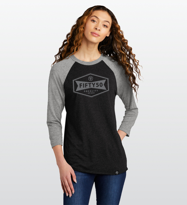 Lady wearing a heather black baseball equality tshirt, with a grey collar and arms, and a grey logo. The logo is a narrow, yet wide hexagon with text that says Fifty50, Equality, Established 2015 inside of it.