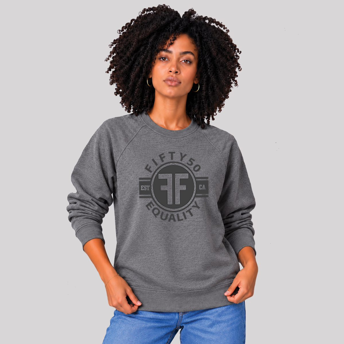 A man wearing a heather grey equality crew sweatshirt. The black graphic says 'Fifty50, Equality'  and has two Fs, back to back in a circle.