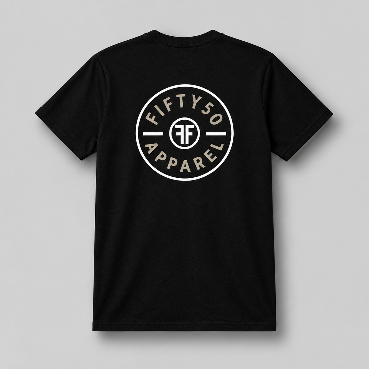 A black short-sleeve t-shirt with a circular white chest graphic that reads 'FIFTY50 APPAREL' with two white FFs back to back in the middle, paired with blue jeans, set against a solid gray background.