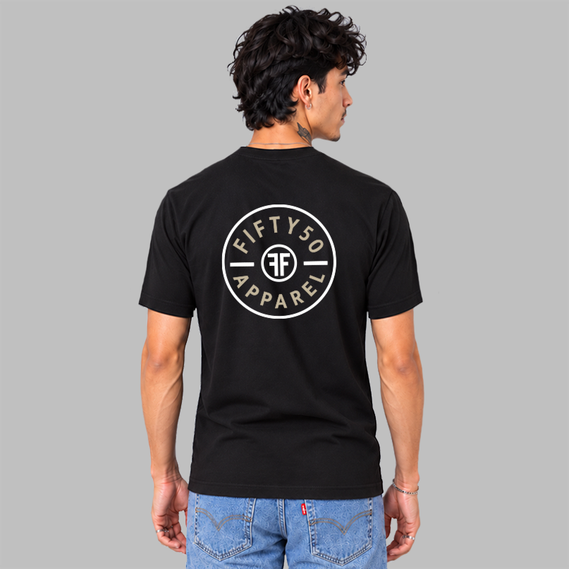 A man viewed from the back wearing a black short-sleeve t-shirt with a circular white chest graphic that reads 'FIFTY50 APPAREL' with two white FFs back to back in the middle, paired with blue jeans, set against a solid gray background.