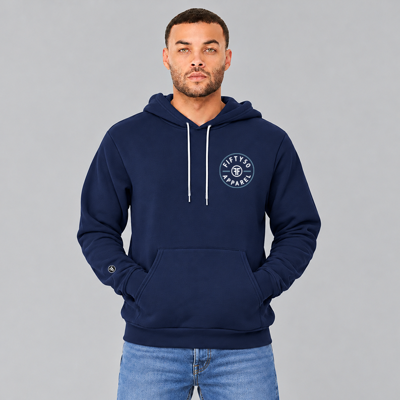 A man wearing a navy blue pullover hoodie with a circular left chest logo graphic that reads 'FIFTY50 APPAREL' in white, with a Slate Blue circle around it. The middle of the graphic has two white Fs back to back.