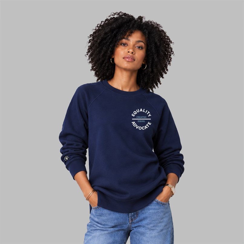 A woman with curly black hair wearing a navy blue crewneck sweatshirt with a white circular 'EQUALITY ADVOCATE' graphic on the chest with 'CREATED EQUAL' in the middle.