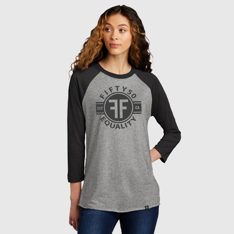 Lady wearing a heather grey equality baseball tshirt with heather black arms and collar. The text of the black graphic says Fifty50, Equality, and has two Fs, back to back in a circle.