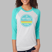 A lady wearing a light grey baseball Pride t-shirt, standing for equality, that has aqua arms and collar. The graphic is round in aqua, orange, green, and yellow, and the text says Fifty 50 Equality, Live Free.