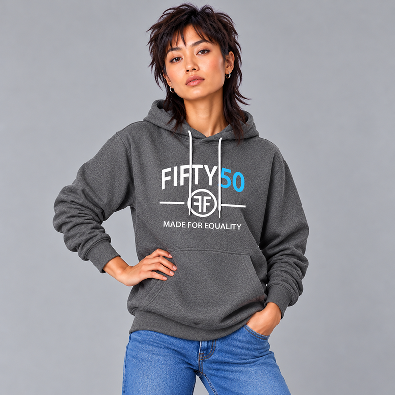 A woman wearing a dark gray pullover hoodie with a white and turquoise graphic print that reads 'FIFTY50 MADE FOR EQUALITY' and two Fs back to back in the middle, paired with blue jeans, against a solid gray studio background.