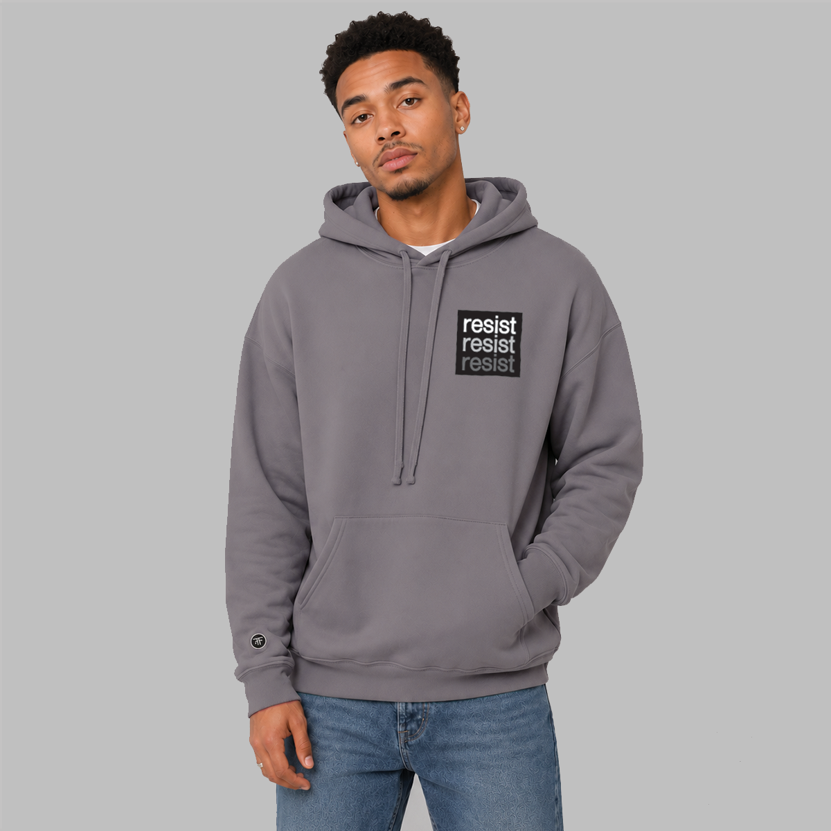 A man wearing a slate purple pullover hoodie with a black chest logo that reads 'resist resist resist' in white, light grey, and dark grey text, paired with blue jeans, against a solid gray background.