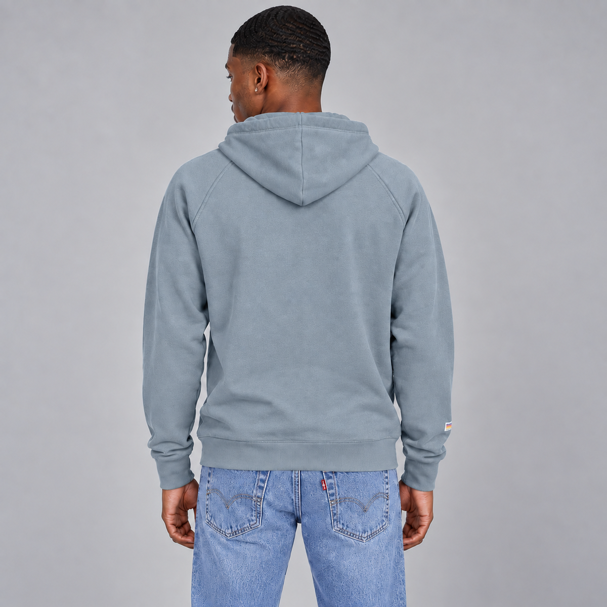 A man viewed from the back wearing a slate blue hooded sweatshirt showing there is no logo and a standard unisex fit.
