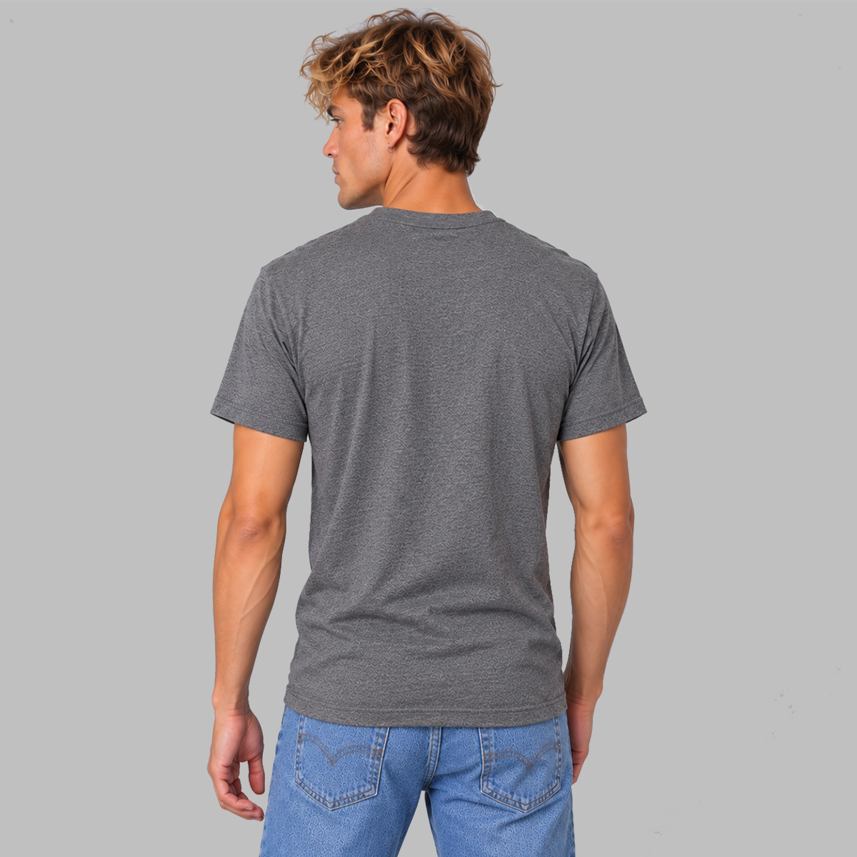 A man viewed from the back wearing a dark heather gray short-sleeve t-shirt showing a unisex fit and that there is no logo on the back. He is wearing blue jeans, and is set against a solid light gray background.