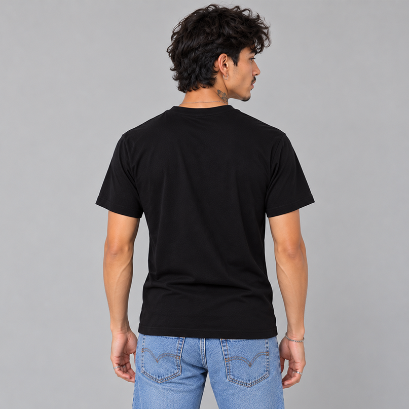 A man wearing a plain black short-sleeve t-shirt, viewed from the back, showing a unisex fit and that there are no graphics on the back, paired with light blue jeans, against a solid gray studio background.