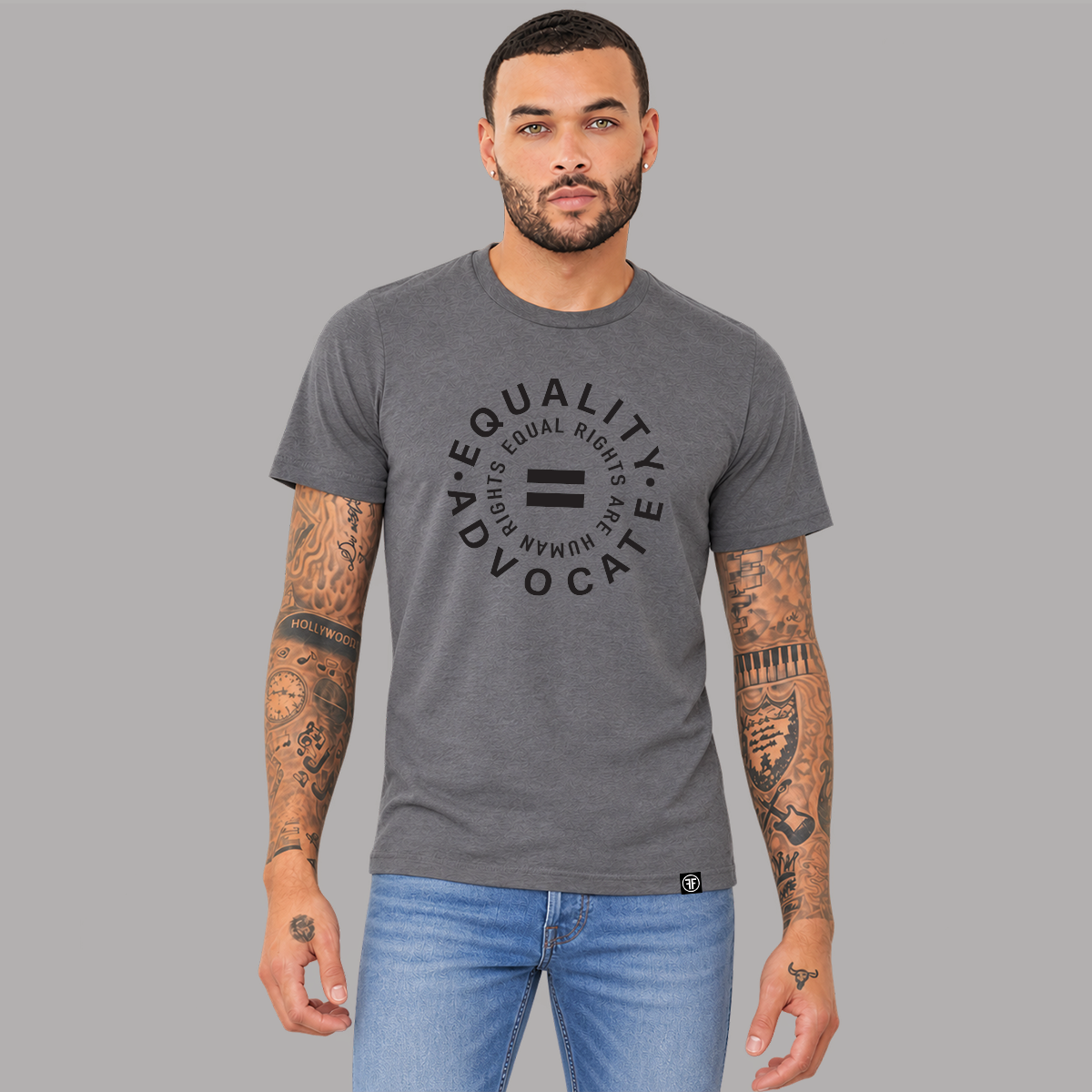 A man wearing a dark heather gray graphic t-shirt with a black circular 'EQUALITY ADVOCATE EQUAL RIGHTS ARE HUMAN RIGHTS' with an equal sign in the middle printed on the chest, paired with blue jeans, set against a solid gray background.
