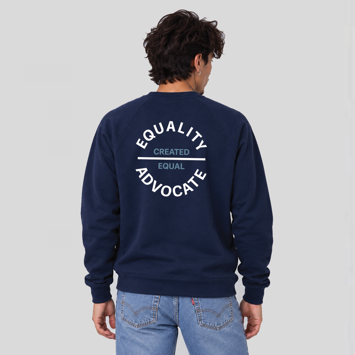 A man viewed from behind wearing a navy blue sweatshirt with a white graphic print on the back reading 'EQUALITY ADVOCATE' and 'CREATED EQUAL' in Stone Blue