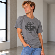 A man wearing a heather gray crewneck t-shirt with a black circular graphic that reads 'FIFTY50 EQUALITY EST. 2025 CA' and light blue jeans.