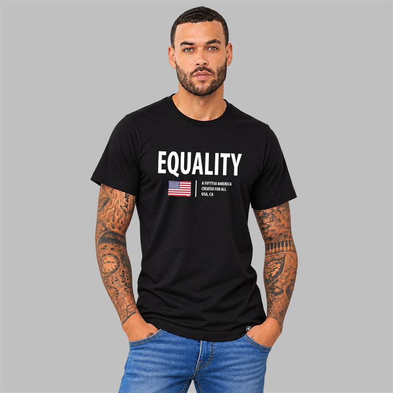 A man with curly dark hair stands in a minimalist white room wearing a black graphic T-shirt with the word 'EQUALITY' in white, a small American flag graphic, and text reading 'A FIFTY50 AMERICA CREATED FOR ALL, USA CA.' 