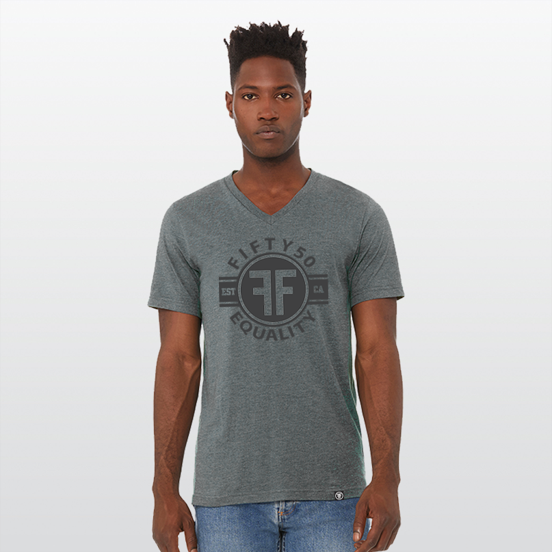 A man wearing a charcoal grey equality vneck tshirt with a black graphic.  The logo text says Fifty50, Equality, and there are two Fs, back to back in the center inside a circle. 