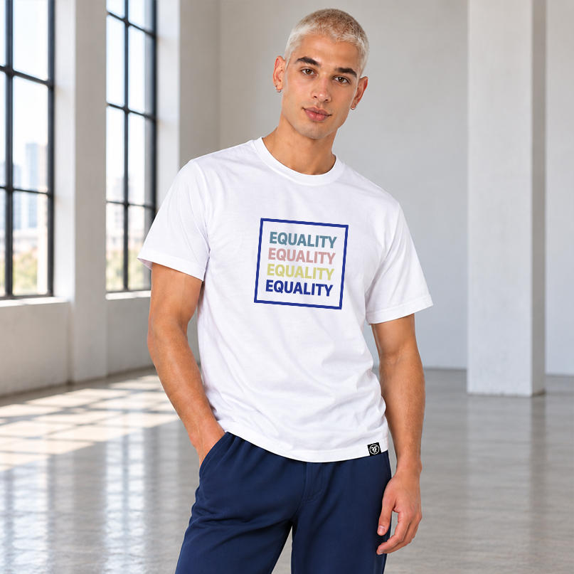 A man wearing a white crewneck t-shirt with a colorful graphic print that reads 'EQUALITY' repeated in stone blue, pink, yellow, and navy blue, paired with navy blue pants sweatpants, standing  a bright, modern studio with large windows.