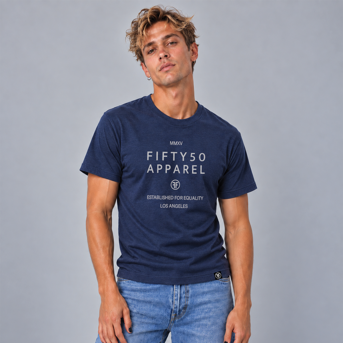 A man wearing a navy blue graphic t-shirt with light grey text reading 'FIFTY50 APPAREL' and 'Established For Equality Los Angeles'