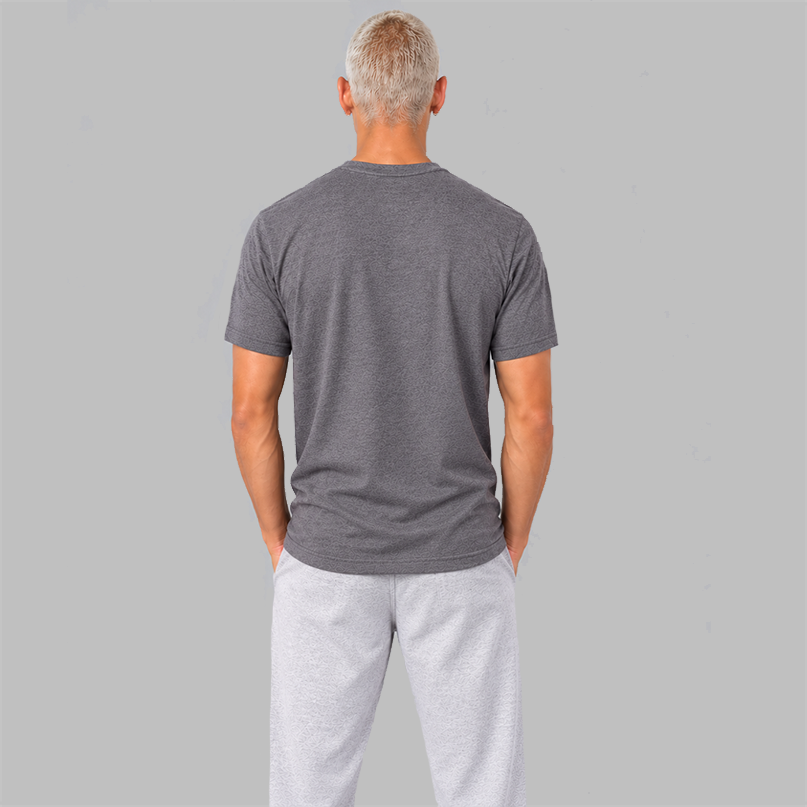 A man viewed from behind wearing a  heather slate purple short-sleeve t-shirt showing a unisex fit and no graphics, paired with light gray sweatpants, standing against a solid gray studio background.