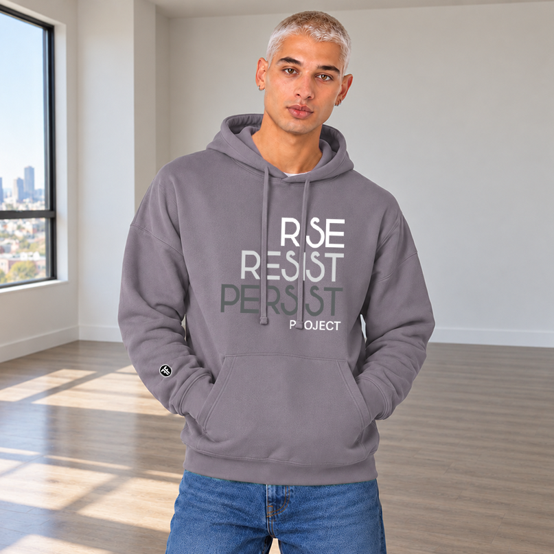 A man wearing a slate purple hoodie with the text 'RISE RESIST PERSIST PROJECT' printed on the front in white, light grey and charcoal grey, paired with light grey sweatpants.