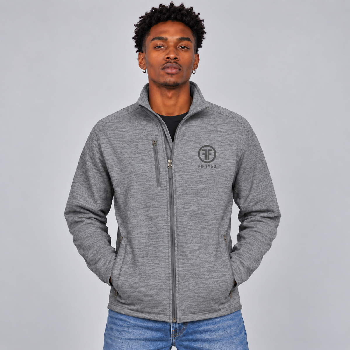 A man wearing a grey jacket with two zippered side pockets, and a zippered right chest pocket. There is a grey embroidered logo on the left chest that has two Fs, back to back, with the text Fifty50