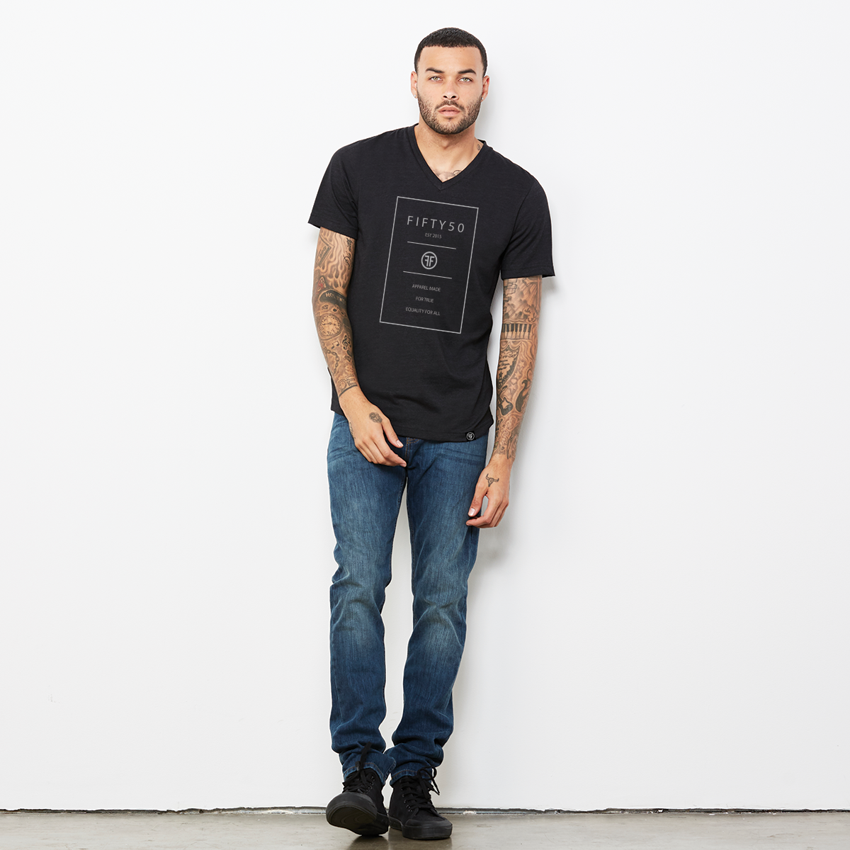 A man wearing a black v-neck t-shirt. The logo is a grey rectangle with the grey text Fifty 50, and Apparel Made For True Equality for All inside of it.