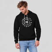 A man wearing a black pullover hoodie with a light grey circular graphic on the chest that reads 'EQUALITY ADVOCATE' and 'PRO WOMEN'S, LGBT, RACIAL RIGHTS, paired with light blue jeans, against a solid light gray background.