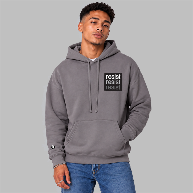 A man wearing a slate purple pullover hoodie with a black chest logo that reads 'resist resist resist' in white, light grey, and dark grey text, paired with blue jeans, against a solid gray background.