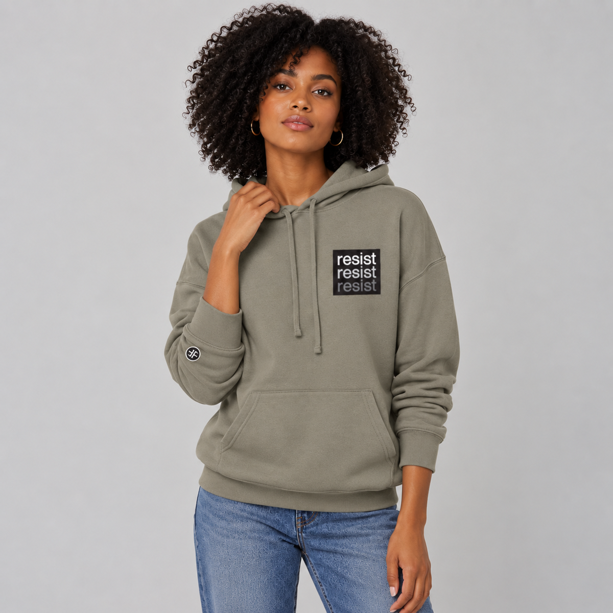 A lady wearing a stone taupe, unisex political hoodie. The logo is a left chest black square, with text that says Resist, three times in white, light grey and dark grey.  