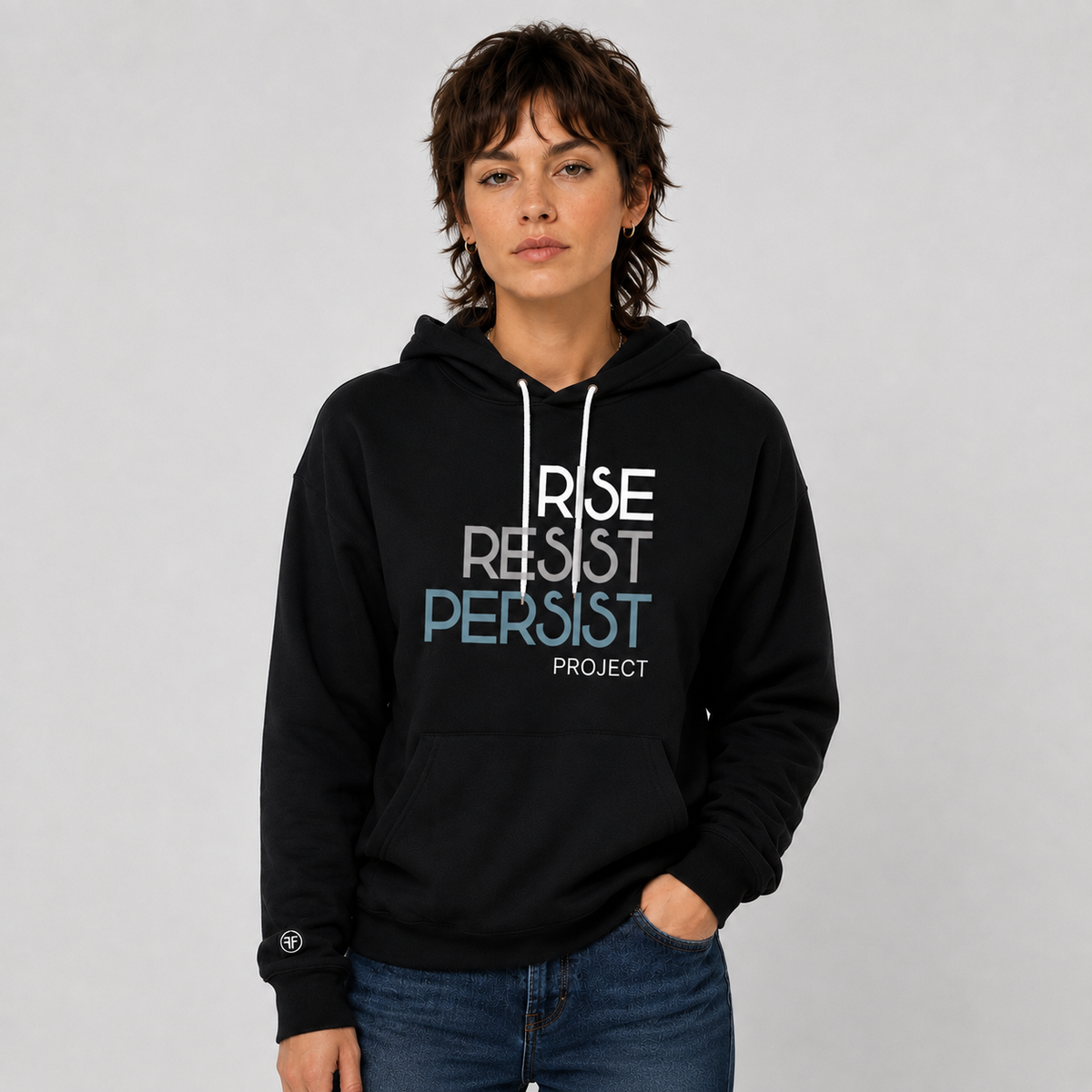 A woman wearing a black pullover hoodie with the text 'RISE RESIST PERSIST' in white, gray, and blue, and 'PROJECT' underneath. She is posing against a neutral gray studio background.