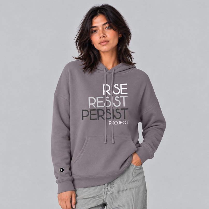 A woman wearing a slate purple hoodie with the text 'RISE RESIST PERSIST PROJECT' printed on the front in white, light grey and charcoal grey, paired with light grey sweatpants.