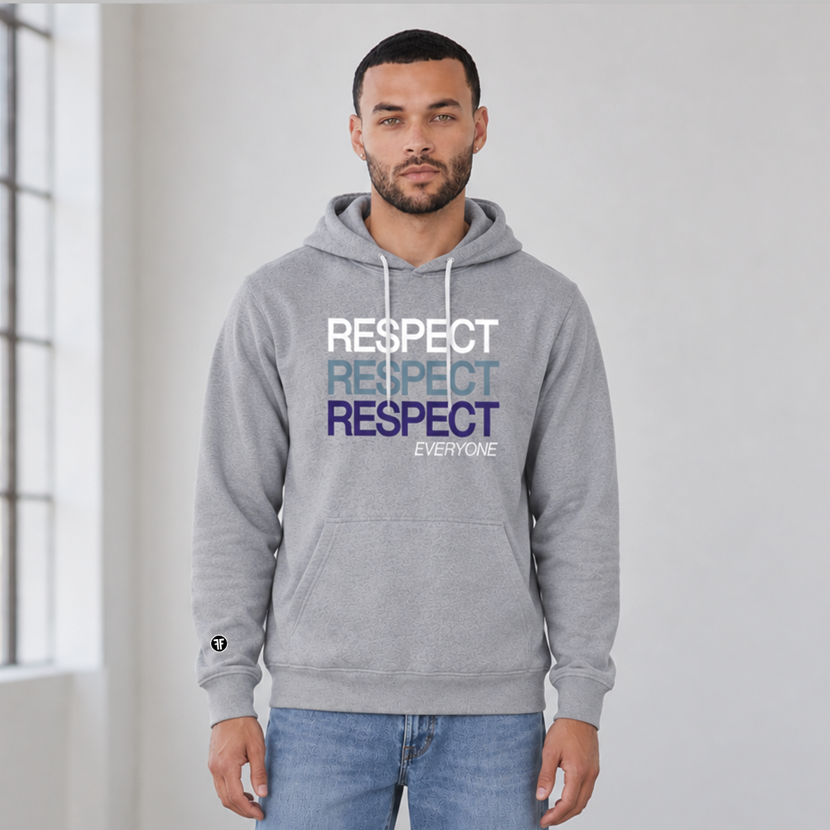 A man wearing an ash gray pullover hoodie with a stacked 'RESPECT' graphic in white, light blue, and navy blue on the chest, paired with blue jeans in a bright, minimalist room.