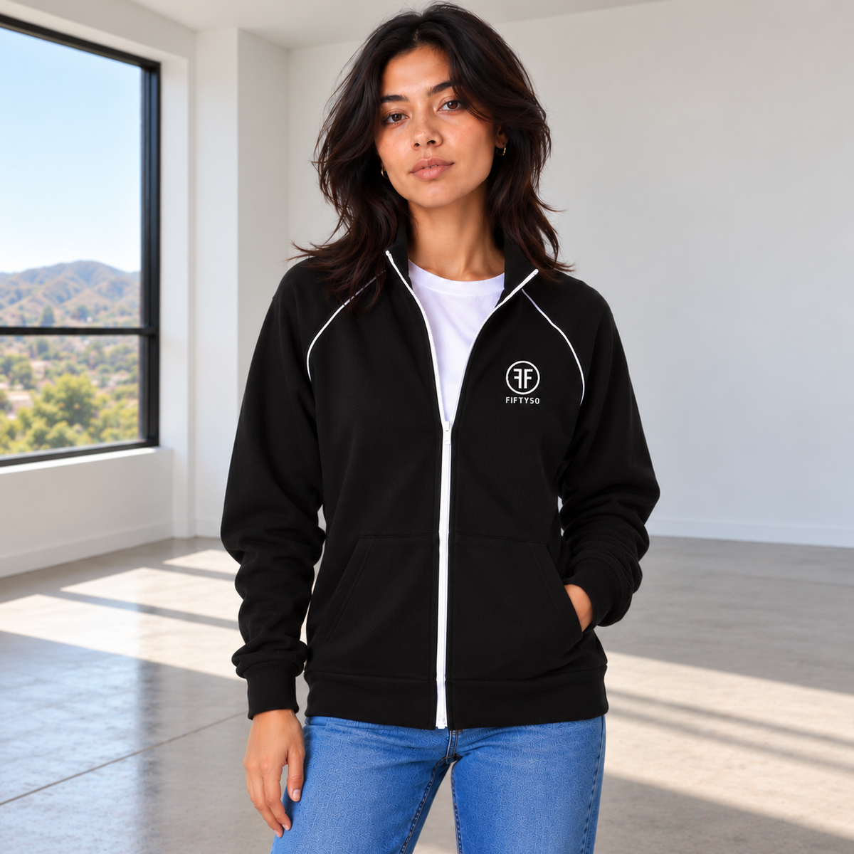 Woman wearing a black jacket with a white zipper and white piping on the front of the shoulders. White embroidered left chest logo, has two Fs back to back outlined by a circle. 