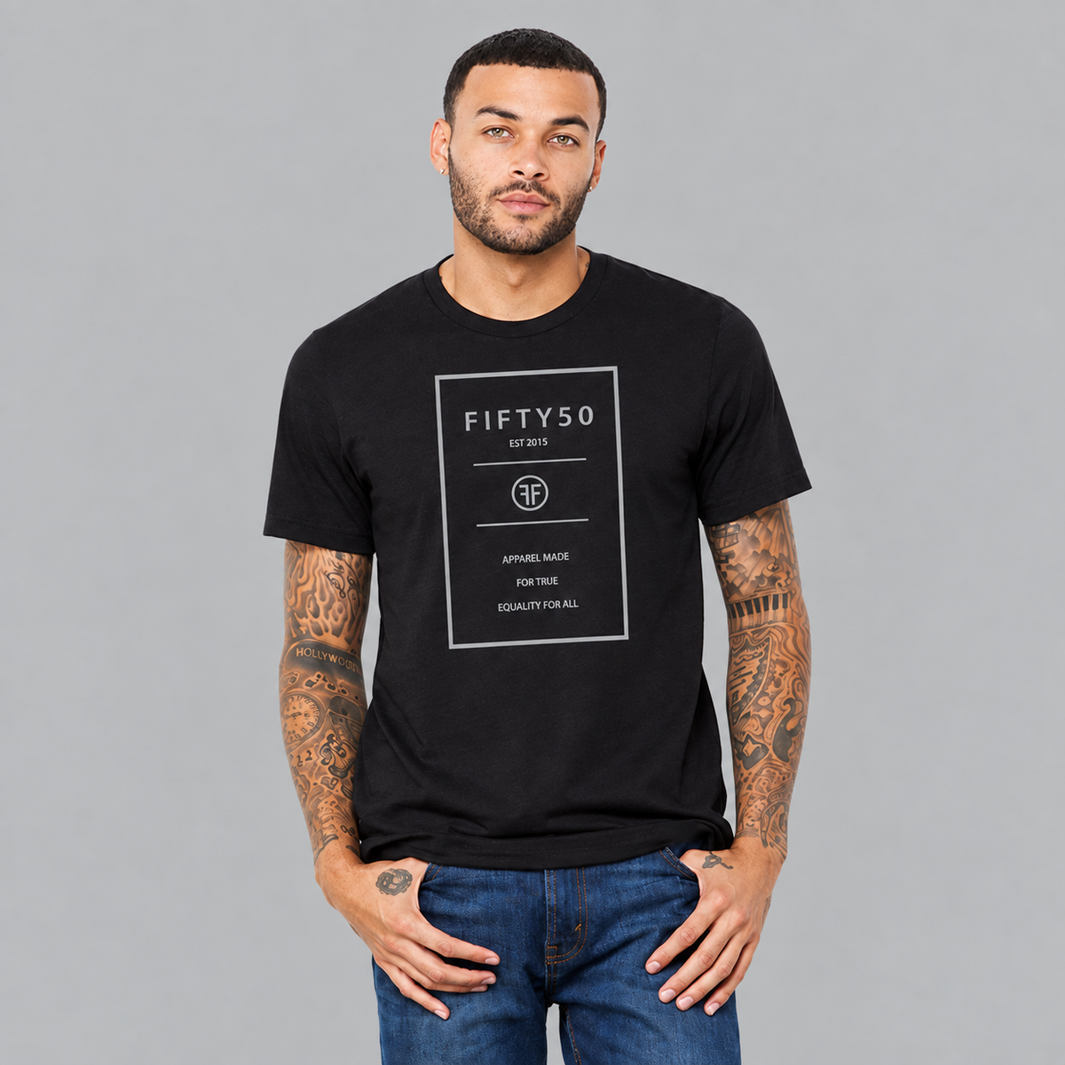A man wearing a black crew t-shirt. The logo is a grey rectangle with the grey text Fifty 50, and Apparel Made For True Equality for All.