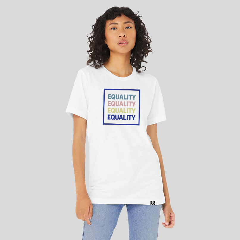 A lady wearing a white equality tshirt with the text Equality, stacked four times in a row, in navy blue, Slate Blue, Dusty Rose, and Bisque Gold. The text is in bold font and is outlined by a navy blue square.  