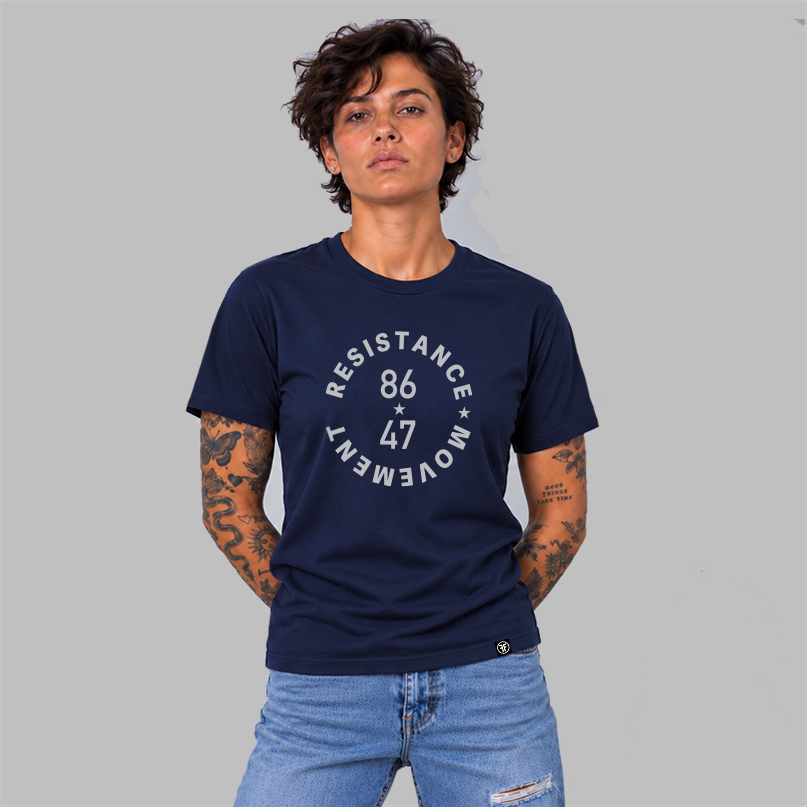 A woman wearing a navy blue t-shirt with a light grey circular graphic that reads 'RESISTANCE MOVEMENT 86 47' on the chest, paired with light blue jeans, set against a solid gray background.