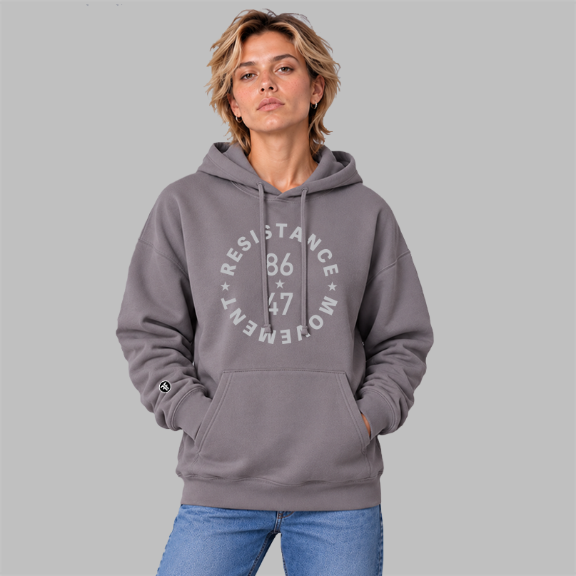 A woman wearing a slate purple colored, unisex political hoodie. The light grey text says "86 47"in the middle with"Resistance Movement" around it.