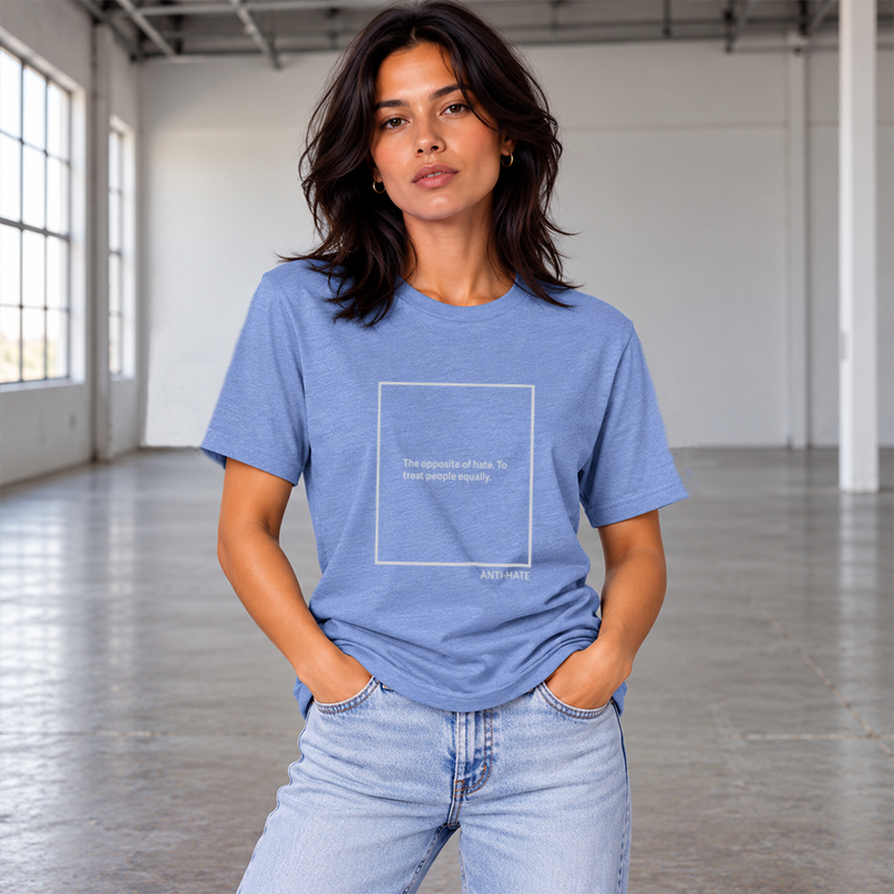 A woman wearing a light blue crewneck t-shirt with a light grey square graphic on the chest containing the text, 'THE OPPOSITE OF HATE. TO TREAT PEOPLE EQUALLY' paired with light wash jeans, set against a solid gray background.