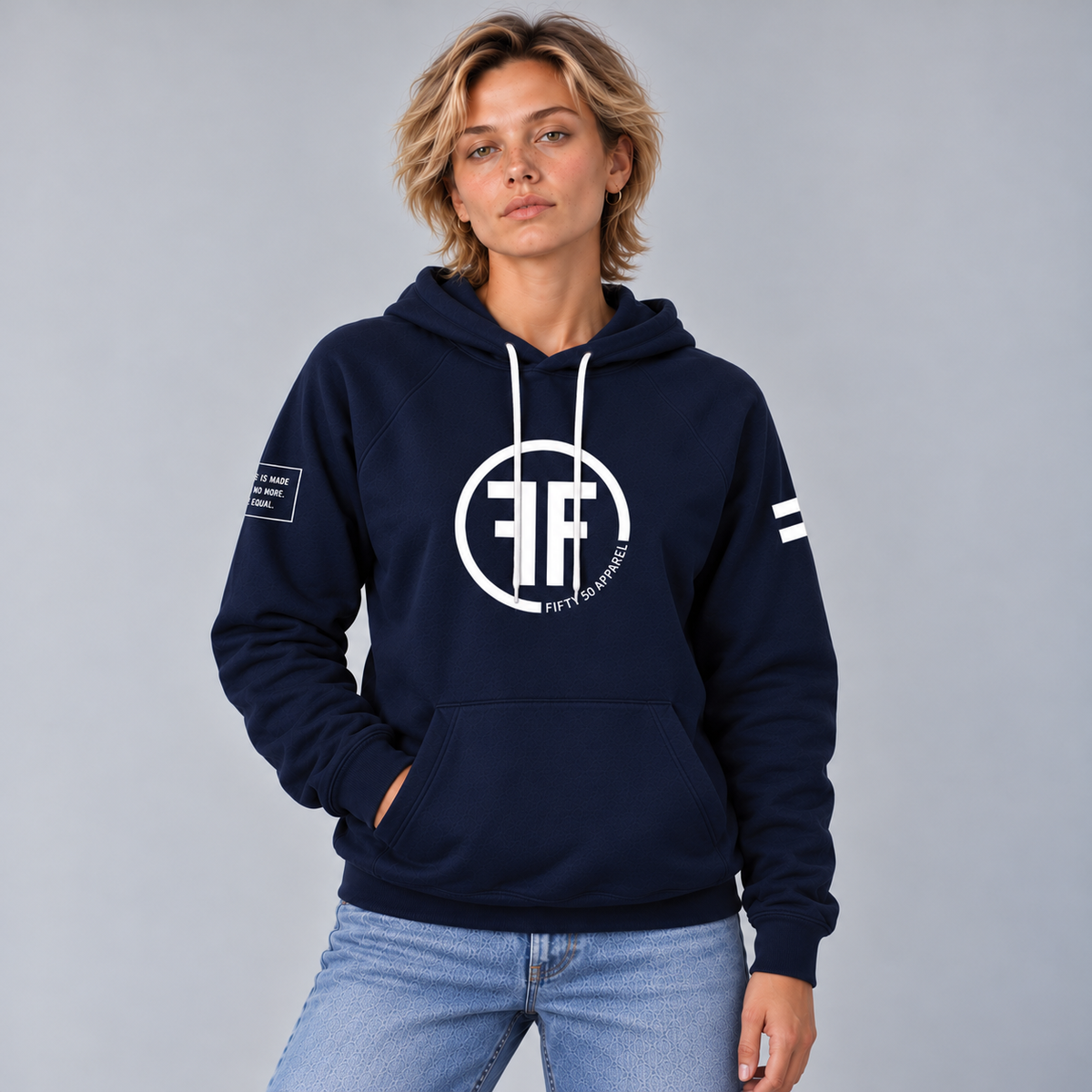 A woman wearing a navy blue equality hoodie with a white equal sign on left arm, and the text, 'Fifty 50 Apparel is made for equality, no more, no less, just equal', on the right arm. Center chest logo has two Fs, back to back outlined by a circle.