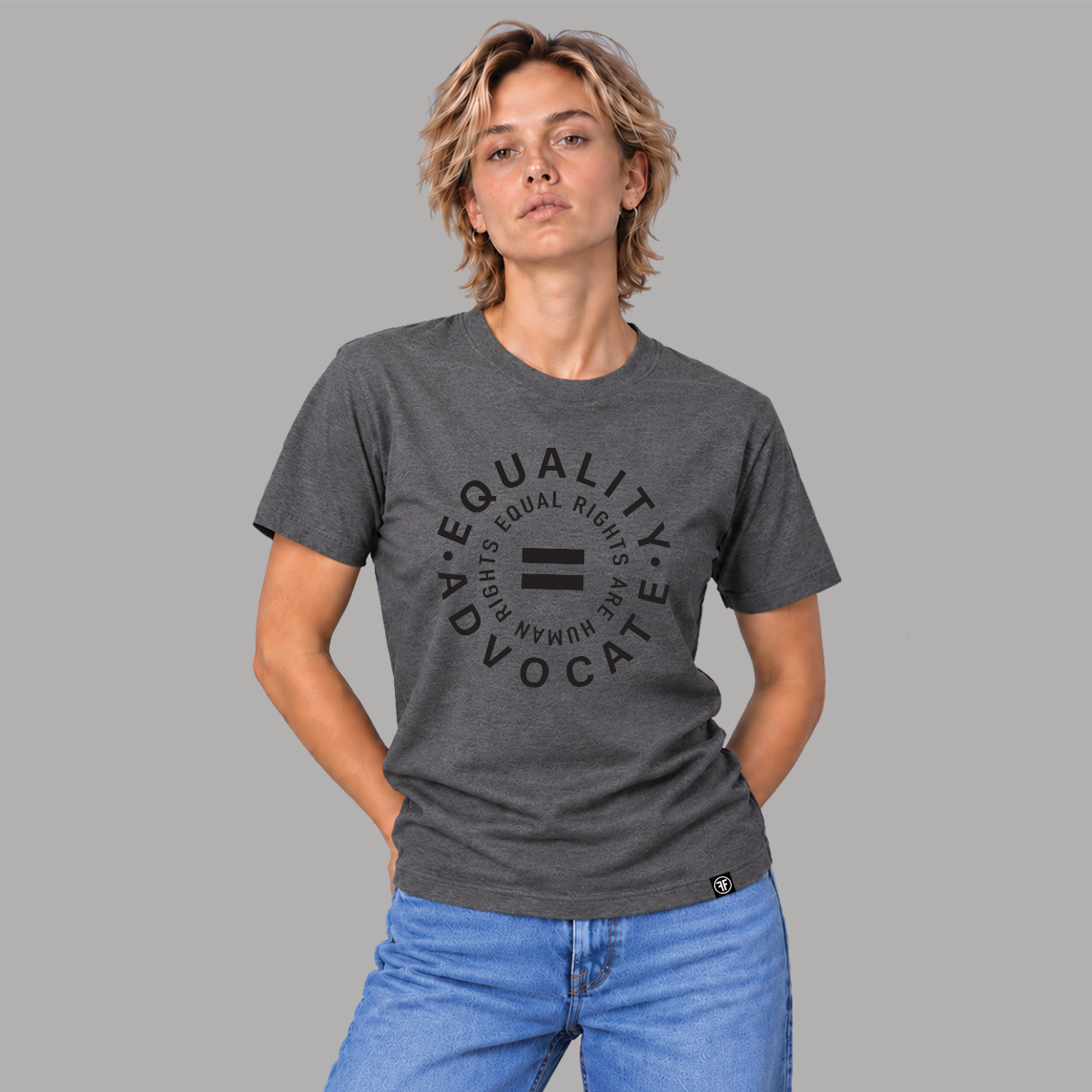 A woman modeling a dark heather gray graphic t-shirt with the words 'EQUALITY ADVOCATE 'EQUAL RIGHTS ARE HUMAN RIGHTS' and an equality symbol printed in black on the front, paired with blue jeans against a solid gray background.