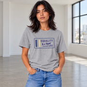 A woman wearing a light ash grey graphic t-shirt with a navy, stone blue, pink and yellow design that says 'EQUALITY IS A RIGHT', 'NO MORE NO LESS JUST EQUAL' with a solid gray studio background.