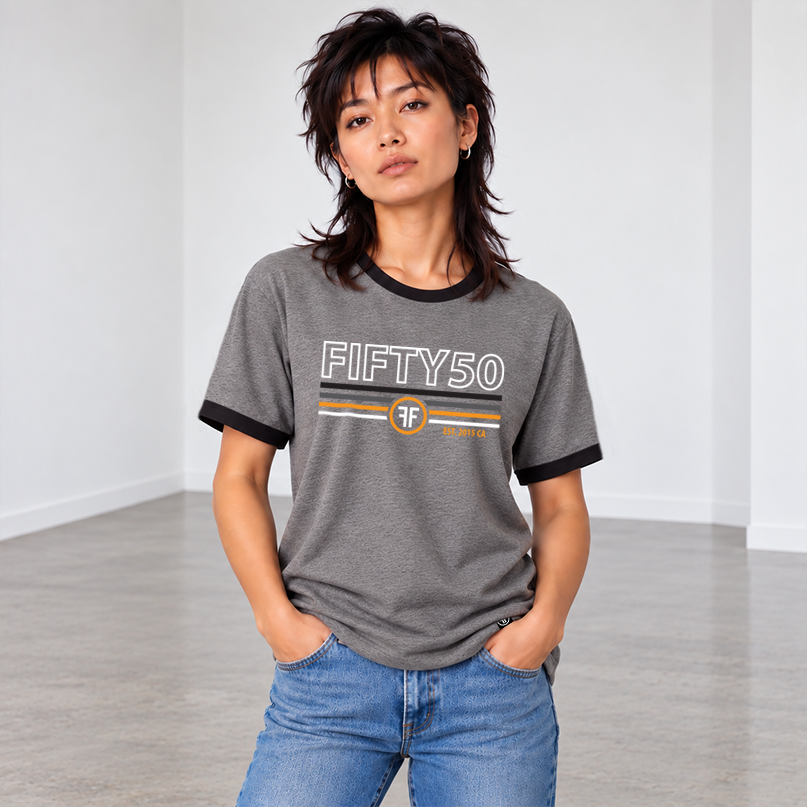 A woman wearing a heather gray ringer t-shirt with black collar and sleeve trim, featuring a 'FIFTY50' graphic with white, orange, and black stripes on the chest.