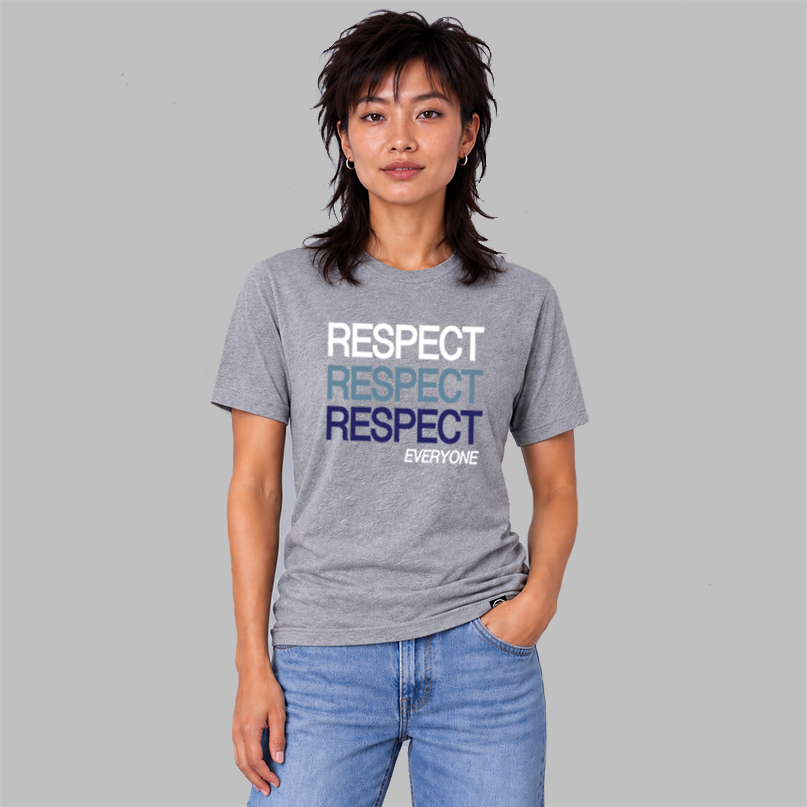 A man wearing a heather gray graphic t-shirt with the word 'RESPECT' printed in white, light blue, and dark blue, paired with light blue jeans, standing in a bright, empty room.