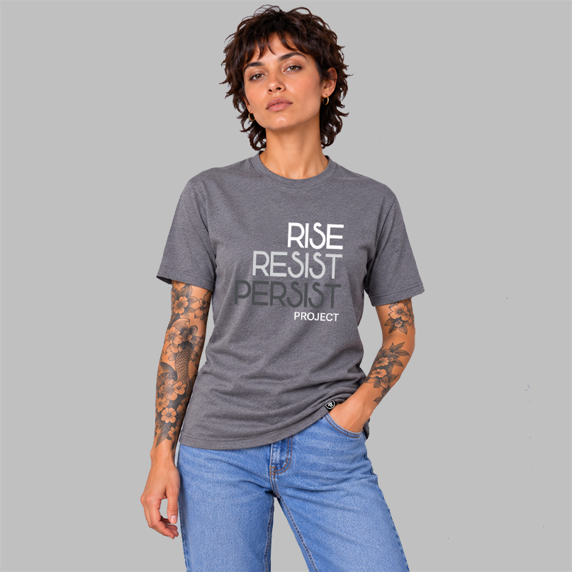 A woman wearing a heather slate purple graphic t-shirt with the words 'RISE RESIST PERSIST' and 'PROJECT' printed on the front in white, light grey, and charcoal grey, paired with light blue jeans, set against a solid gray background.
